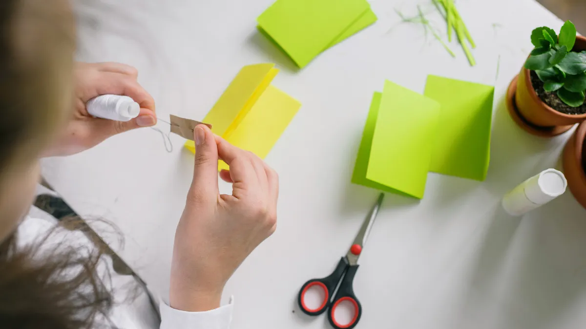 Hands folding colored paper with scissors on a craft table