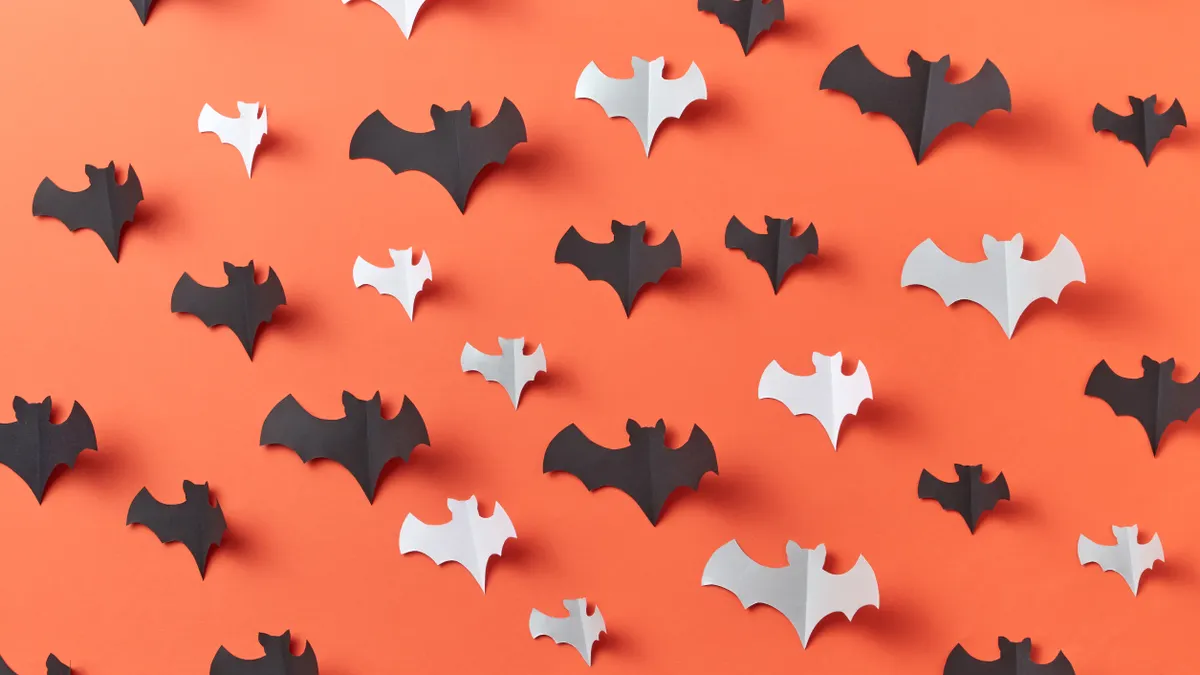 Scattered paper bat cutouts on orange