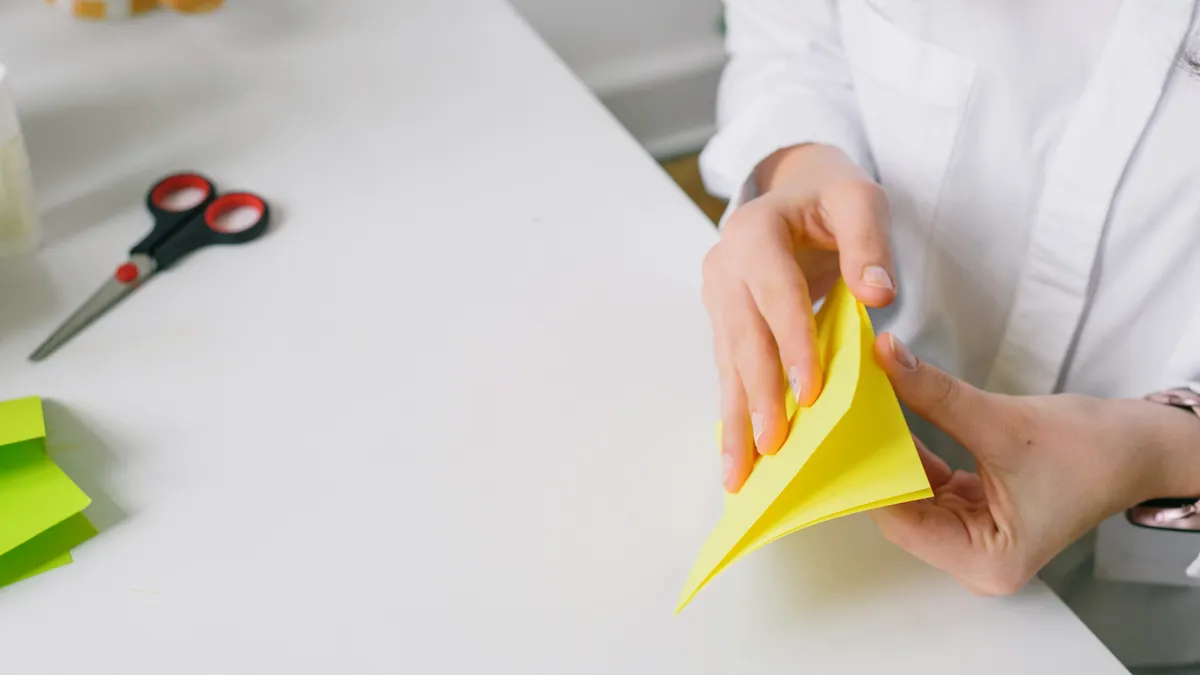 Person folding yellow paper at a table