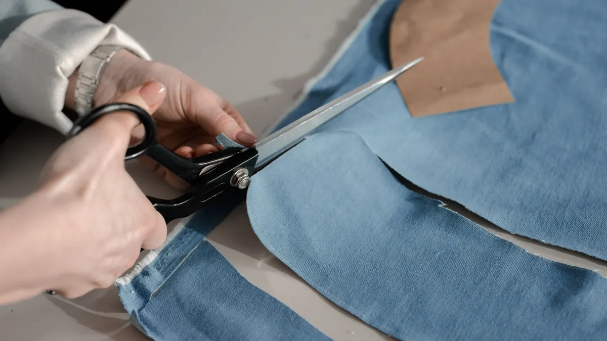 Hands cutting blue fabric with scissors