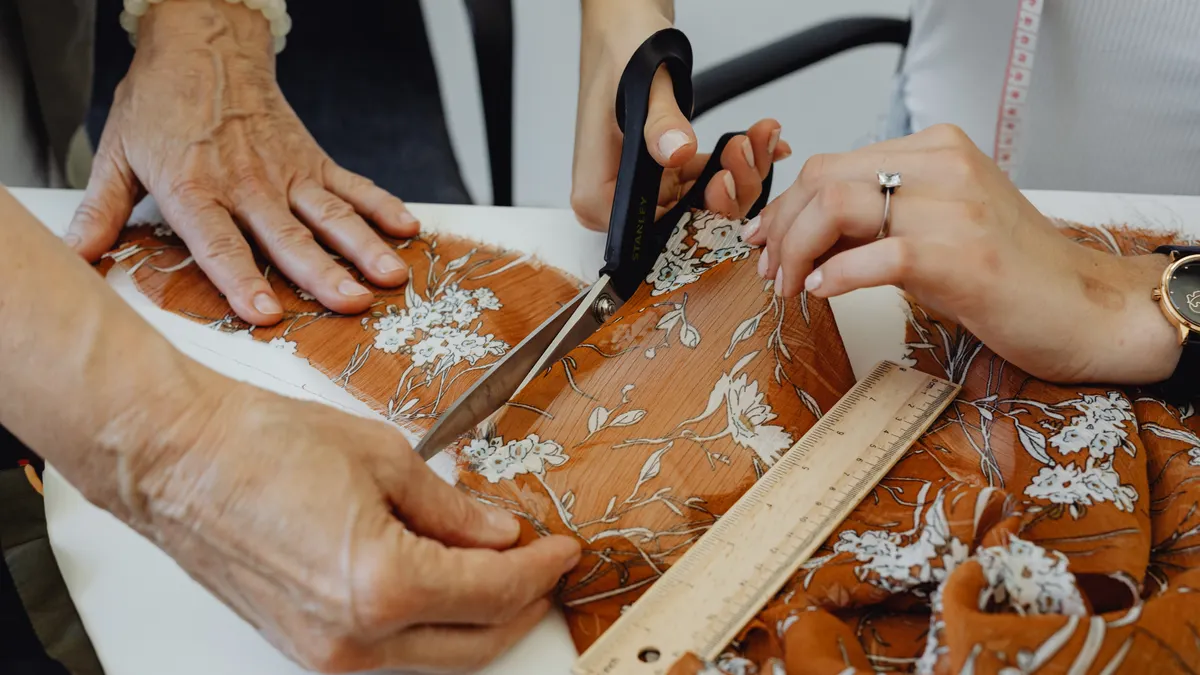 Hands cutting patterned fabric with scissors and ruler